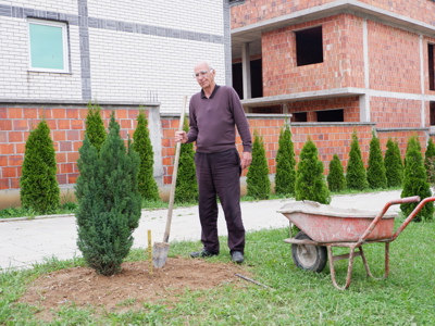 A man plants a tree outside of a house in Arllat village in Kosovo
