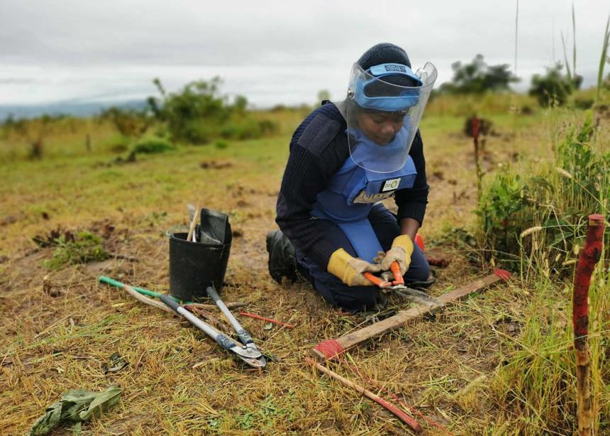 Female deminer wears PPE whilst carrying out demining activities on the ground