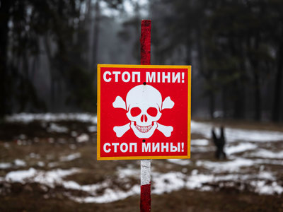 A red danger mines sign with a skull and crossbones and message in Ukrainian standing in a snow covered minefield
