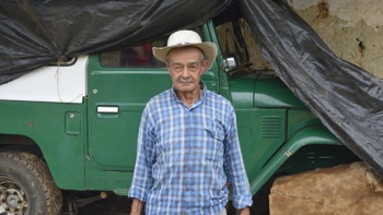 A Colombian farmer stands in front of a large jeep like vehicle