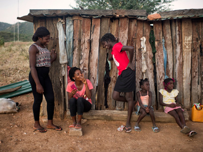 Women talk outside whilst two children sit close by