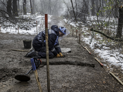 A deminer excavates the soil whiles wearing PPE in a snowy mine marked area