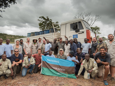 HALO and National Geographic Staff stand in front of HALO vehicles and hold the National Geographic flag