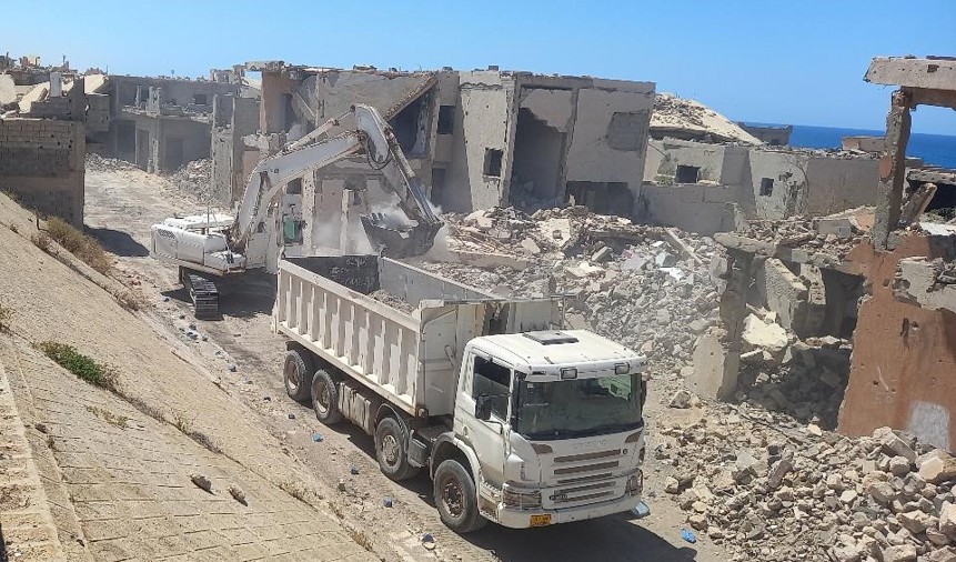An armoured digger scoops rubble into the back of a lorry in Sirte, Libya