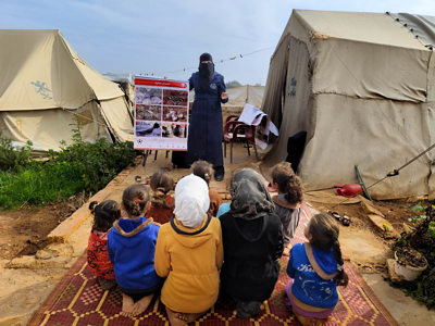 Kids sit on a rug outside listening to a HALO risk educator 