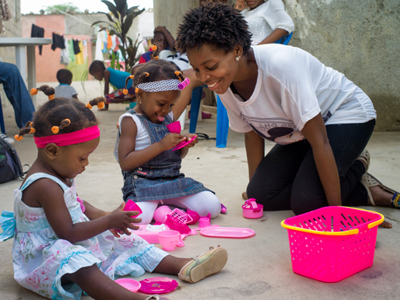 Zana Soares, mother of two daughters, smiles with her babies as they play with toys on the ground