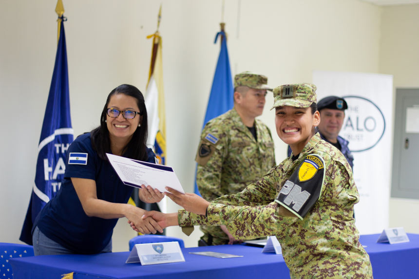 Two smiling women shaking hands as one hands a certificate of training completion to the other