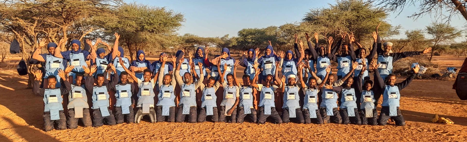 A group of deminers pose in line and celebrate with their hands in the air