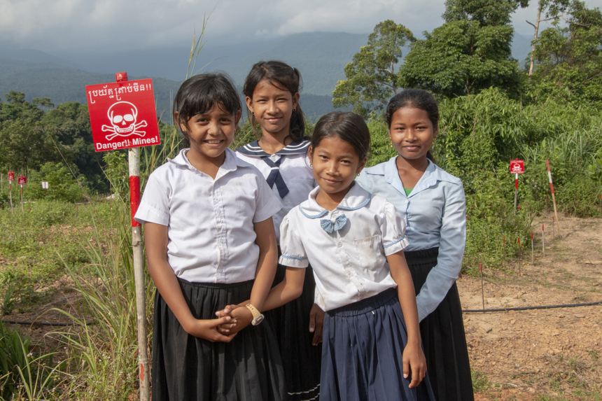 Four children pose in front of a minefield with warning signs in Cambodia