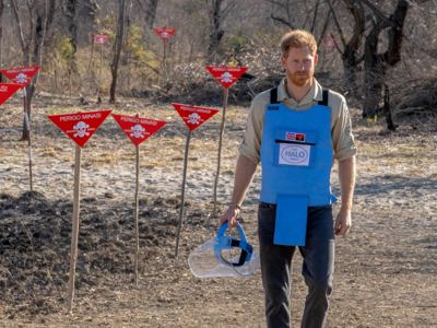 Prince Harry walks through a minefield in Angola, wearing PPE and holding a visor next to red danger signs