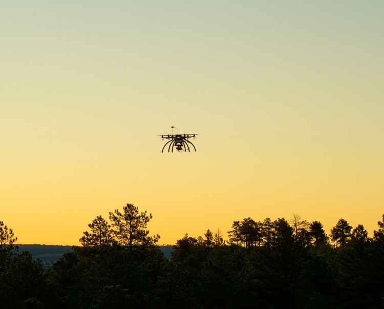 A drone flying over the treeline during sunset