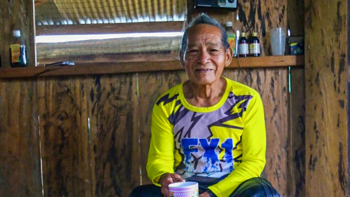 Don Lauro sits on a bench wearing wellies and holding a tea cup