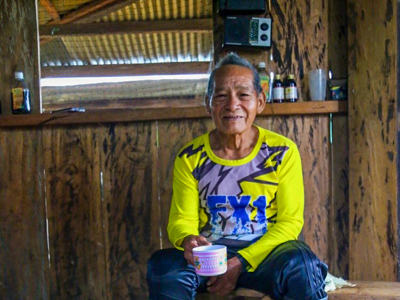 Don Lauro sits on a bench wearing wellies and holding a tea cup