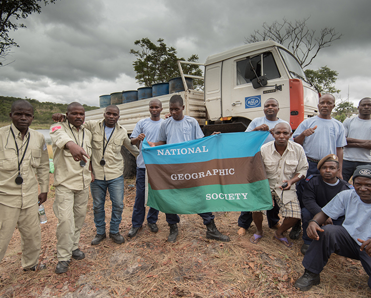 Male HALO workers pose with a flag of the national geographic society