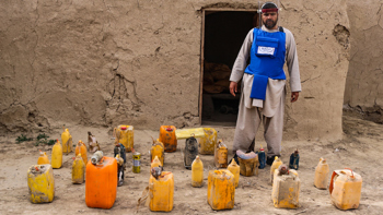 HALO Trust deminer in protective gear, standing next to unearthed improvised explosive devices (IEDs)