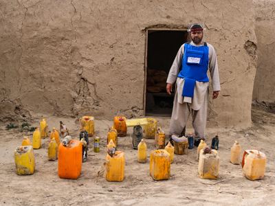 HALO Trust deminer in protective gear, standing next to unearthed improvised explosive devices (IEDs)