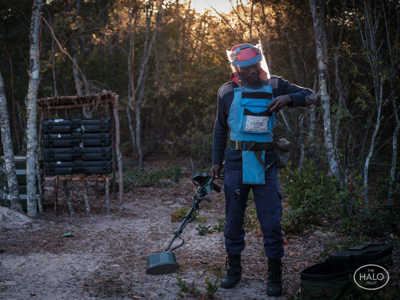 Deminer wearing PPE stands whilst holding a metal detector in Cuito Cuanavale
