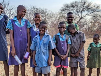 A group of children in school uniform smile in a rural area